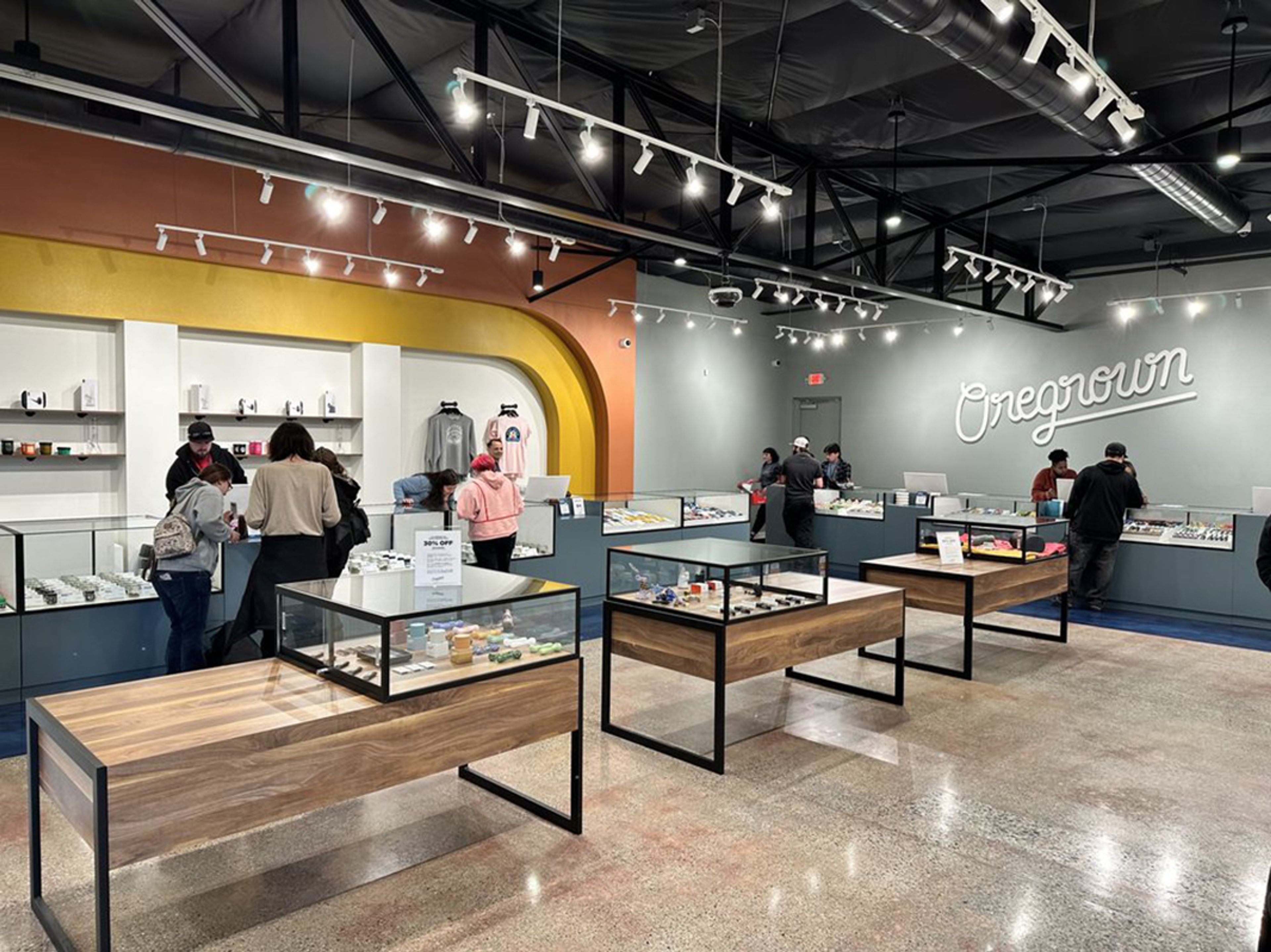 Large room with display tables in foreground and shelves with products behind, Oregrown logo on the side wall, people looking at products.