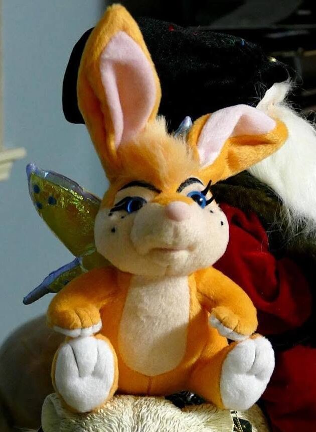 Plush toy of a bunny with large ears, blue eyes, and a cheerful expression, sitting with arms and legs out.