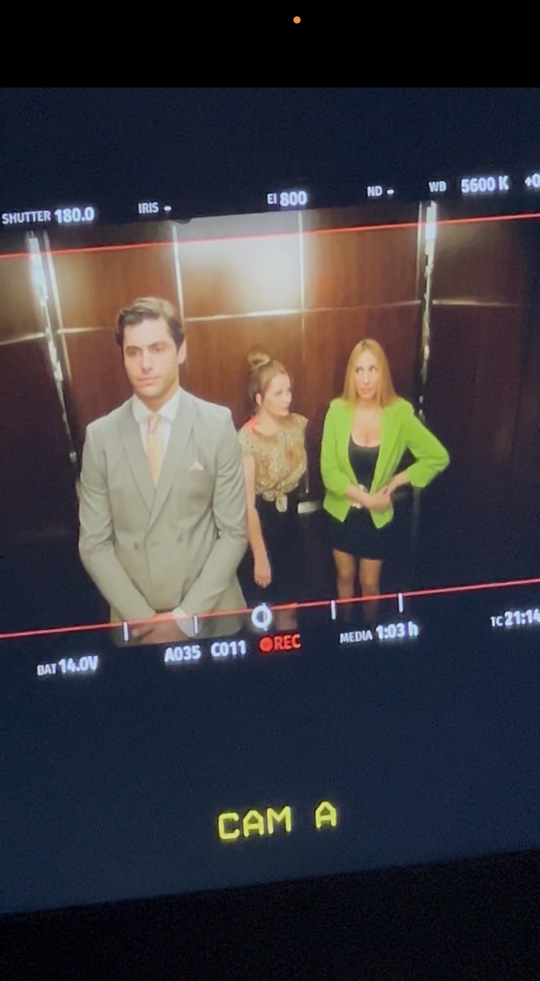 Three people standing in front of a reflective background, two women and one man, dressed formally.