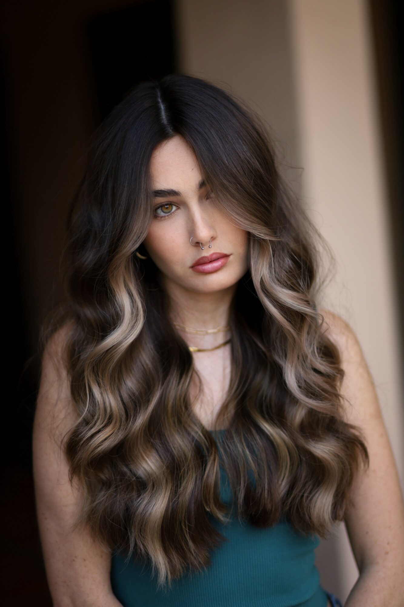 Young woman with long, wavy hair and a serious expression, wearing a teal top, indoors.