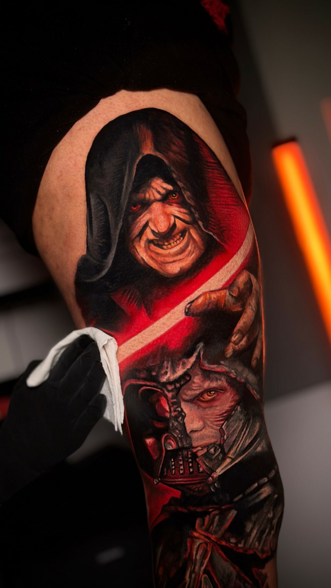 Tattoo of a screaming face with dark hair and a red background on a person's arm.