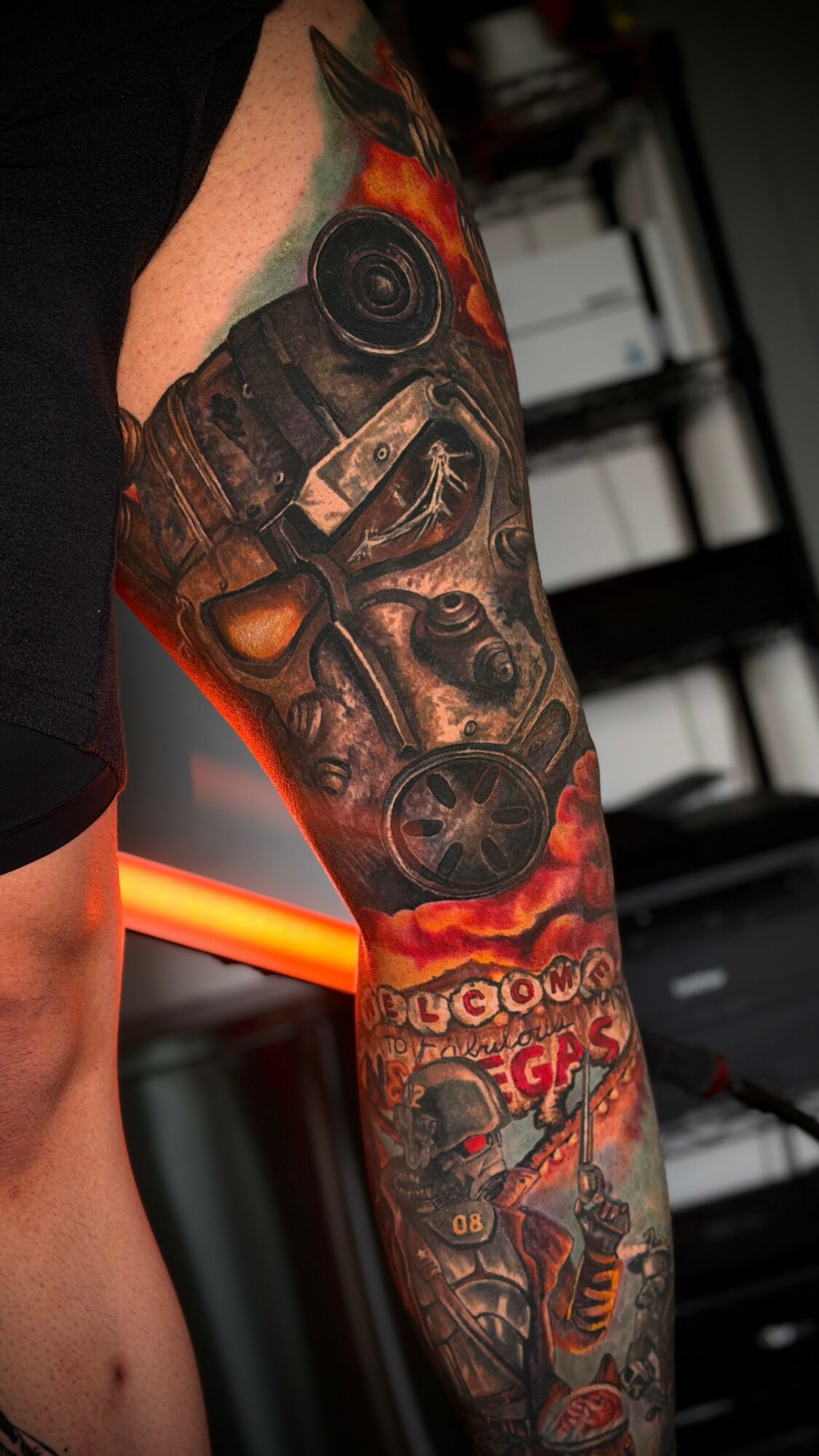 Tattooed arm with a detailed design including a gun, flames, and a skull, with vibrant colors and intricate shading.