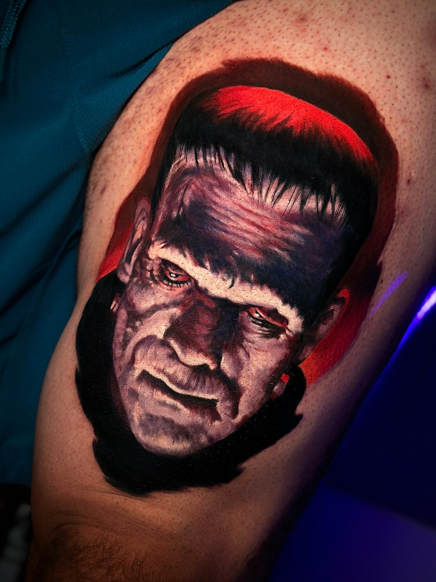 Tattoo of Frankenstein's monster's face with dark hair and a serious expression on a person's arm.