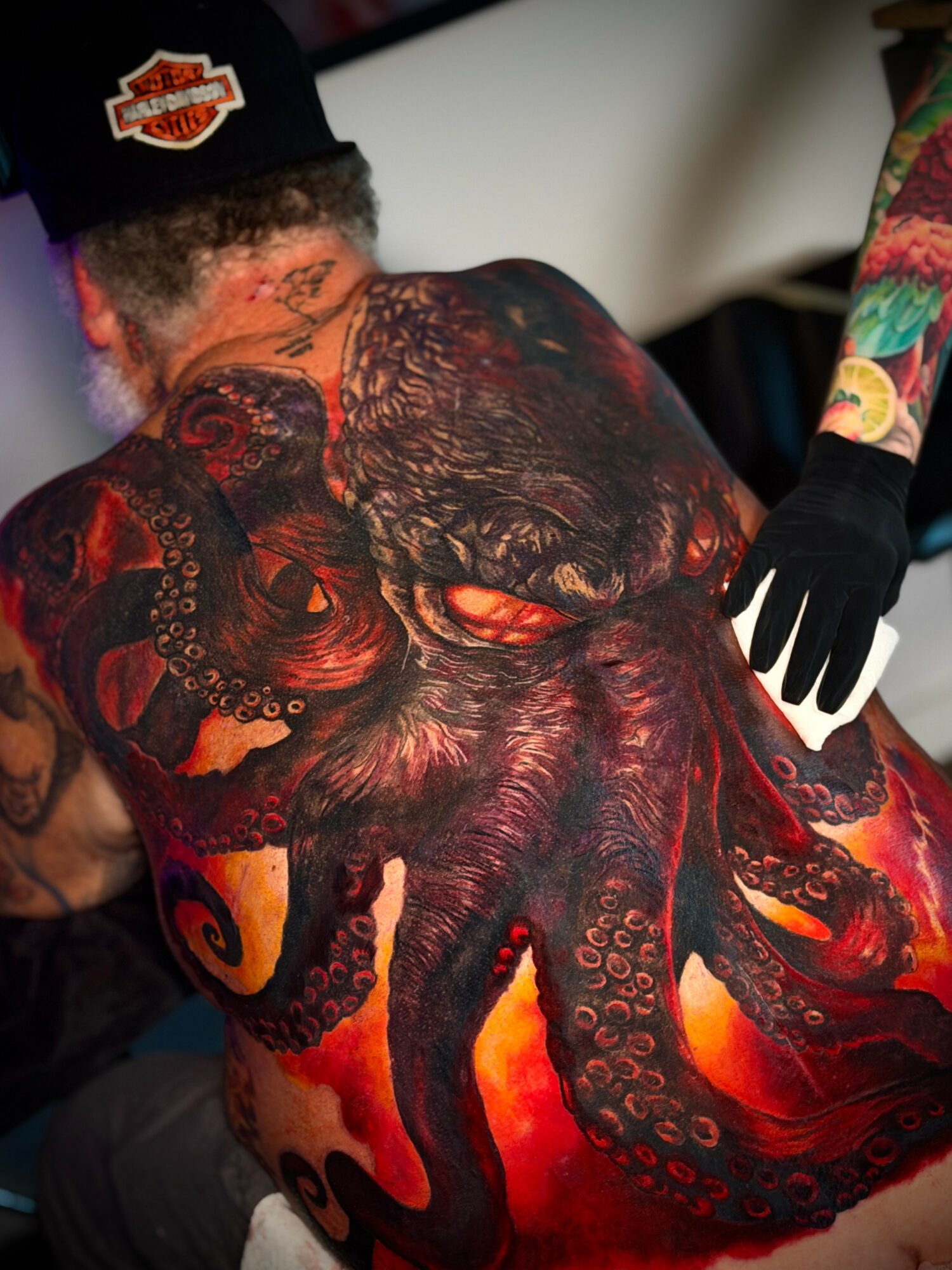 Person with a detailed octopus tattoo covering their back, with a tattooed arm and a gloved hand visible.