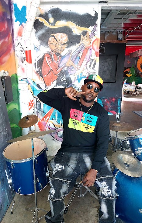 dre-in-front-of-drums-pic-and-mural-obsidiian, Obsidian Healing Camp is rejuvenating minds in deep West Oakland, Culture Currents Featured 