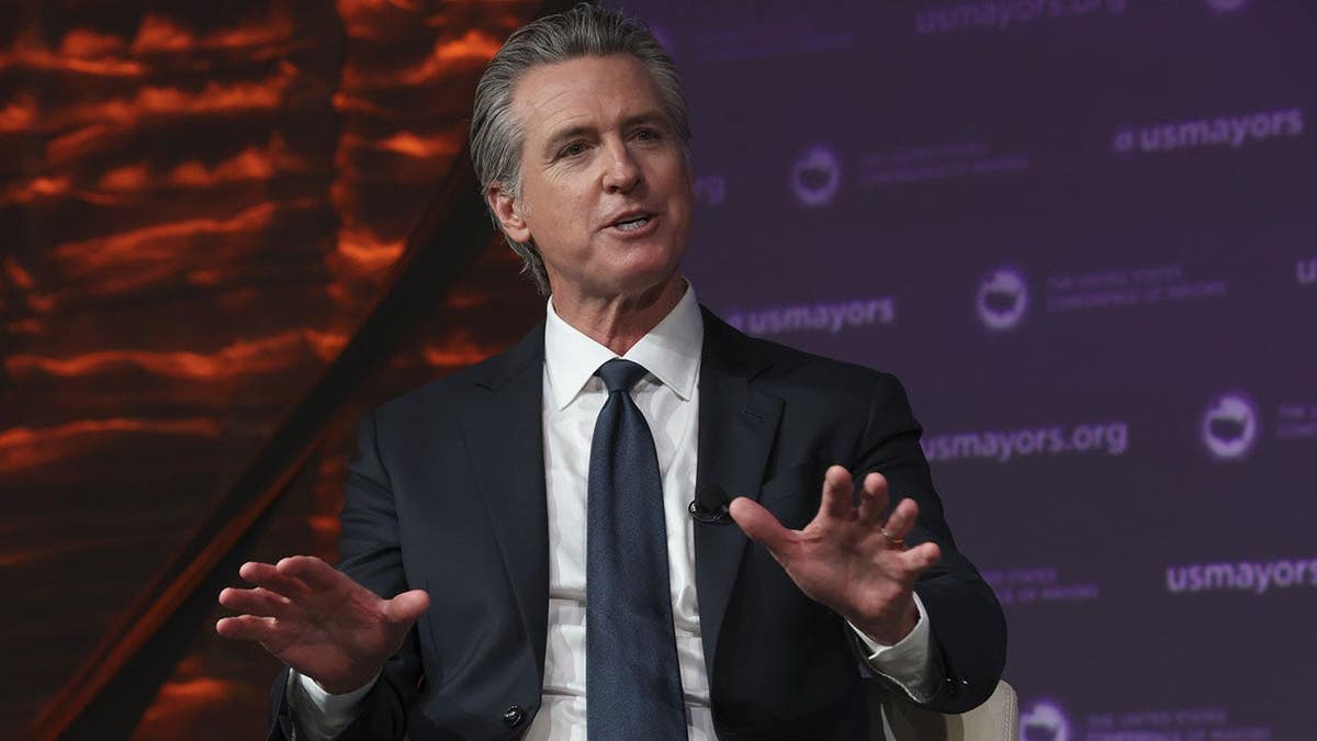 Governor Gavin Newsom standing at a podium at the United States Conference of Mayors meeting in Long Beach, California