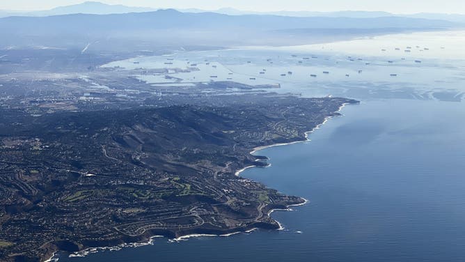 An aerial image taken on October 28, 2021 shows the Palos Verdes Peninsula (L) and cargo container ships (back) waiting in the Pacific Ocean to unload at the Port of Los Angeles and Port of Long Beach as seen above the coast of Palos Verdes, California.