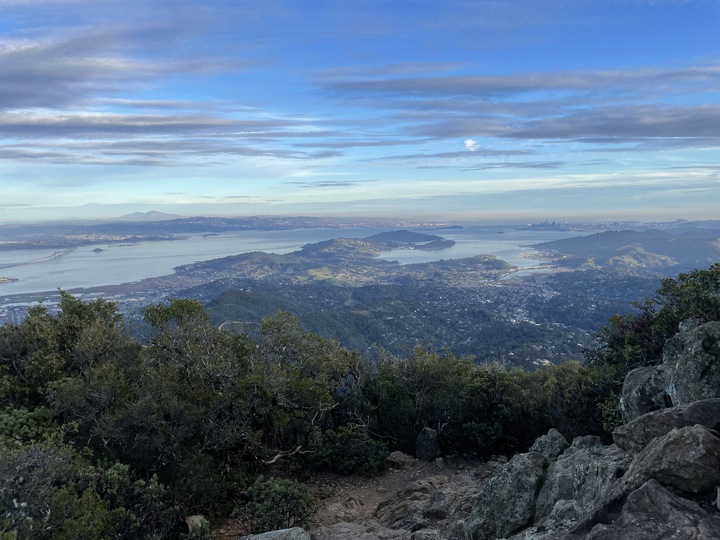 A rocky pile on the right gives way to a vast view of the Bay and some green hills next to it.
