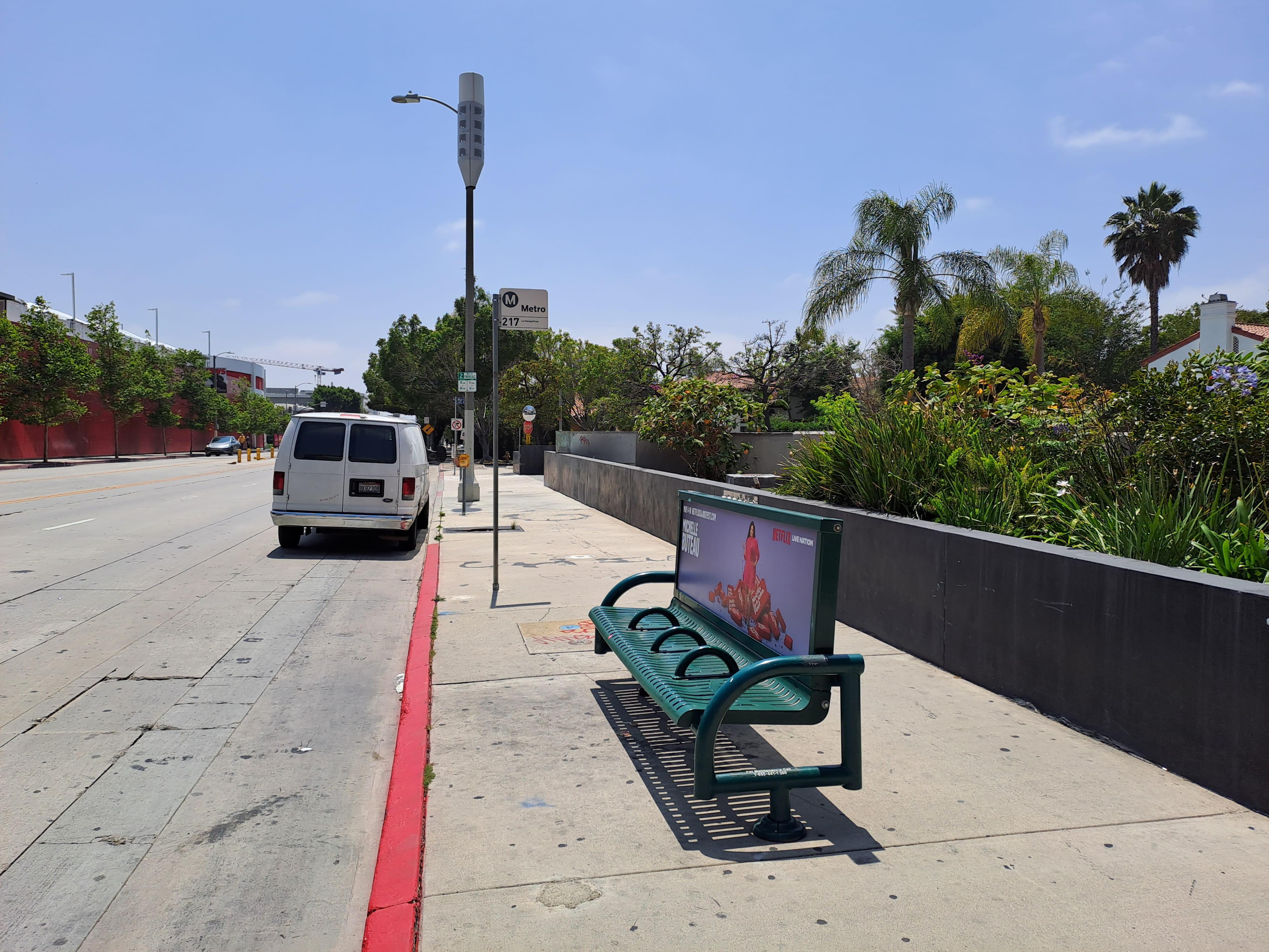 A bench sits on a sidewalk in the sun