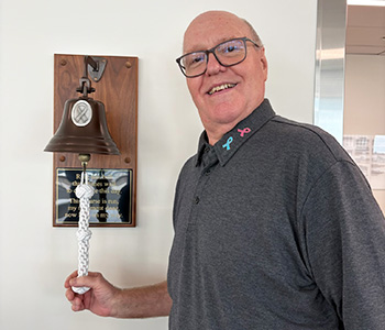 Prostate cancer survivor Michael Brill, wearing a gray shirt, rings the cancer-free bell at the Chao Family Comprehensive Cancer Center in Irvine on July 1, 2026.