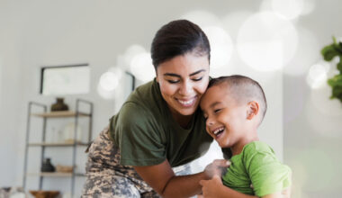 A person in a green shirt and camouflage-patterned pants leans near a young child, appearing engaged in a playful interaction.