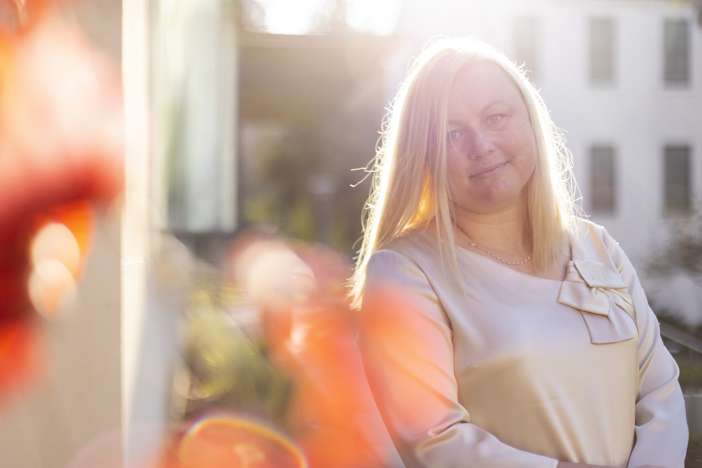 Kate Karniouchina standing outdoors in late-day sunlight, backlit with orange foliage in the foreground.