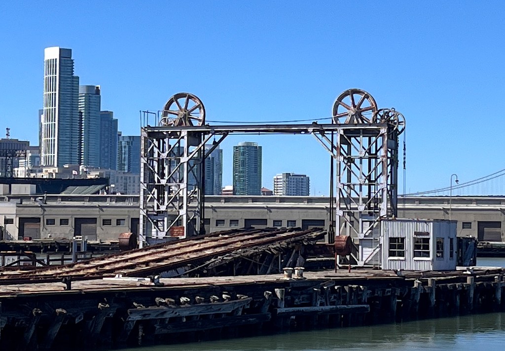 A steel and wood structure with an elevated rail bed and downtown SF in the background. 
