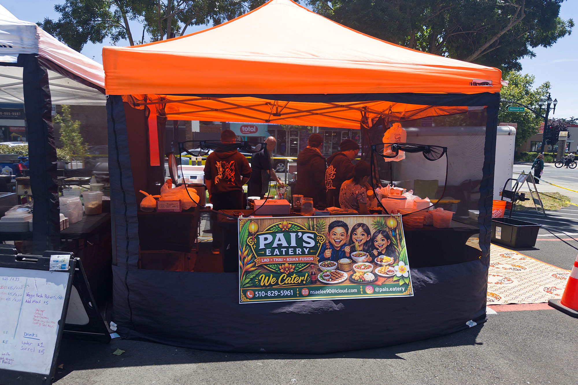 An orange food tent at a street food market. The sign reads, "Pai's Eatery."