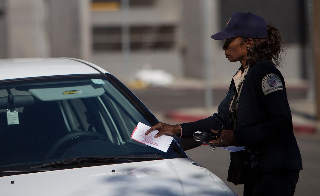 A parking enforcement officer puts a ticket on a car.