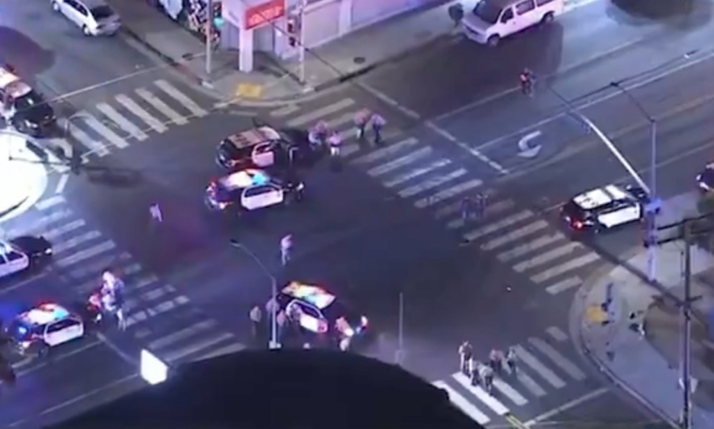 Aerial view of an intersection with multiple police cars and officers investigating a shooting.