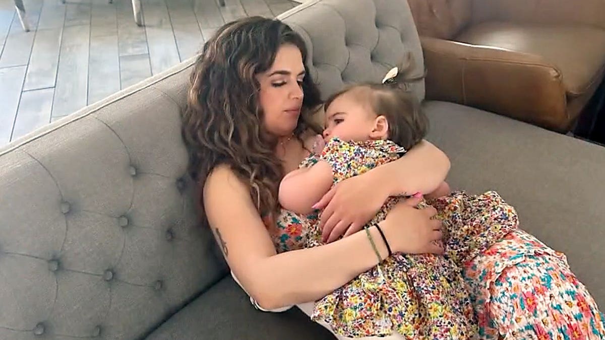 Ivana Balistreri cradles her daughter, Lilliana, while sitting on a couch.