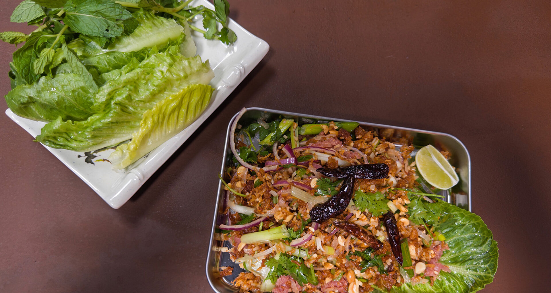 Lao ricd ball salad, served on a metal tray with a plate of fresh herbs and lettuces on the side.