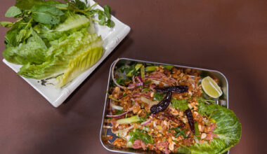 Lao ricd ball salad, served on a metal tray with a plate of fresh herbs and lettuces on the side.