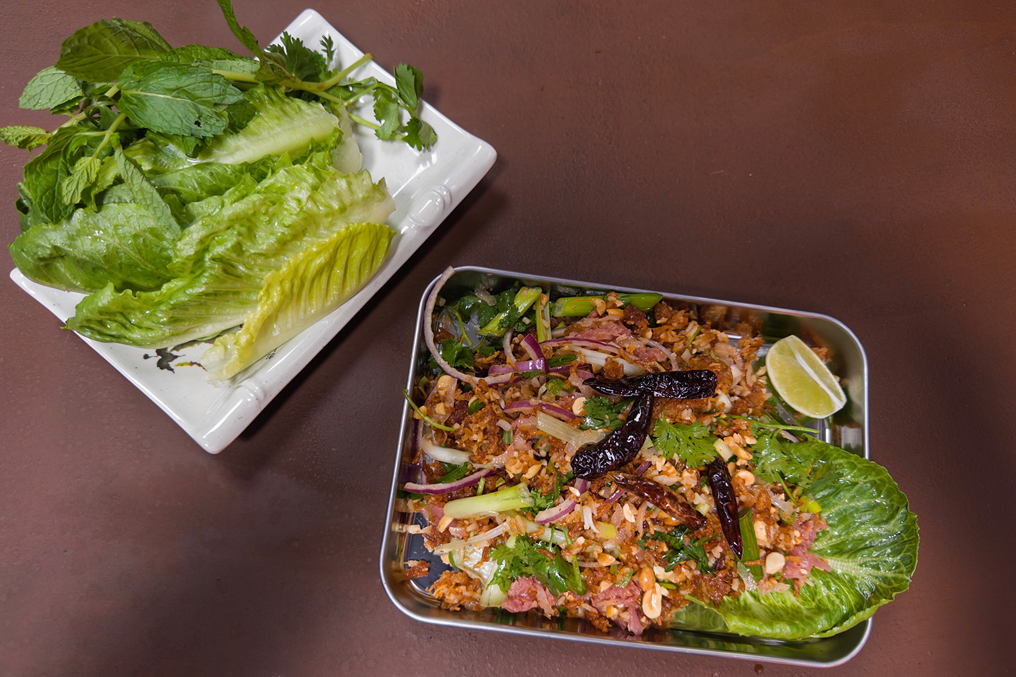 Lao ricd ball salad, served on a metal tray with a plate of fresh herbs and lettuces on the side.
