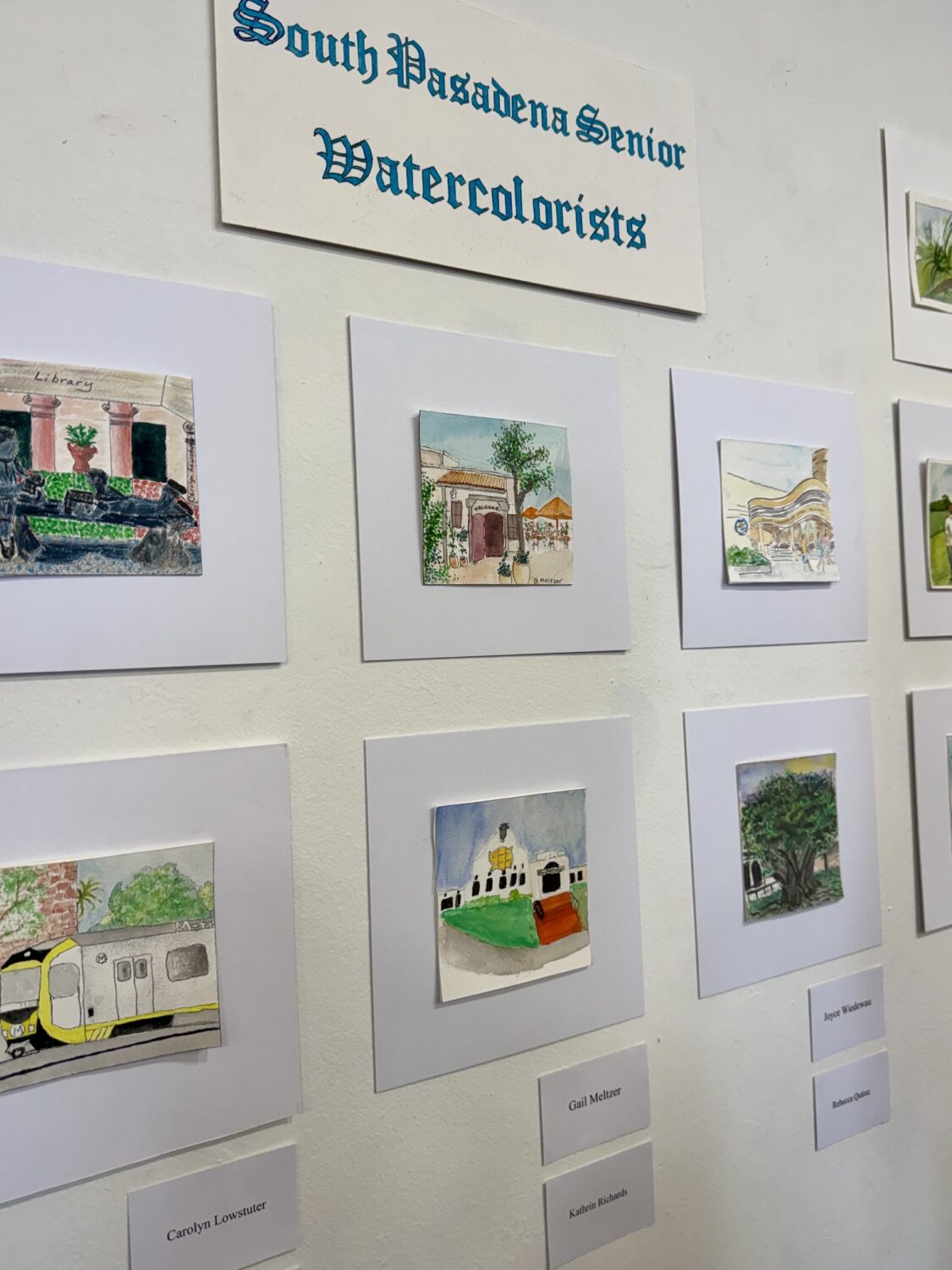 Wall display of small watercolor paintings mounted on light gray mats, labeled'South Pagadena Senior Watercolists'