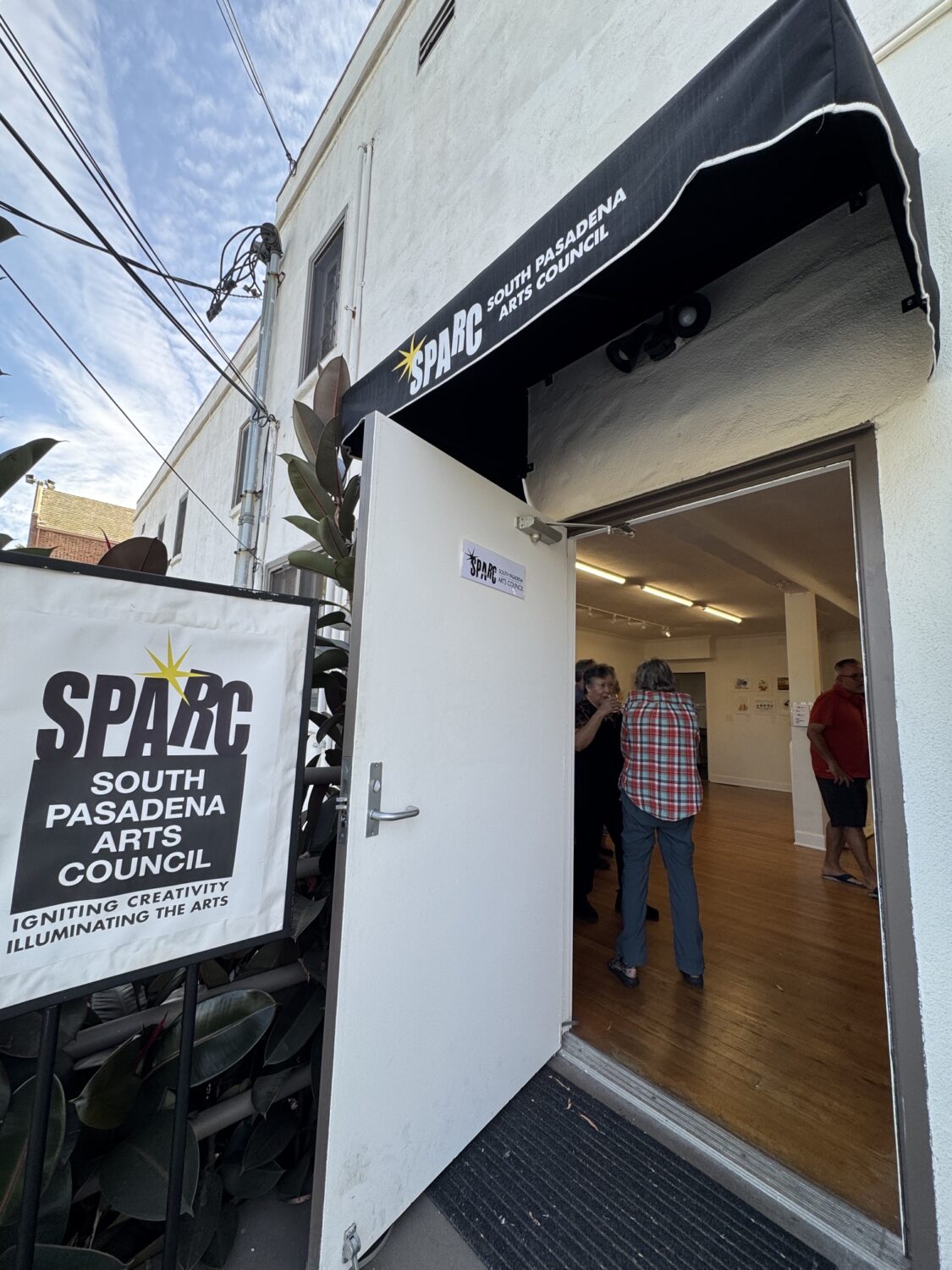 Entrance to SPARC South Pasadena Arts Council with a black awning; open door showing people inside talking.