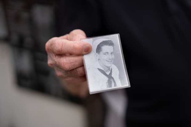 Standing at the Mt. Soledad National Veterans Memorial, Bob McCollum pulls out a photo of himself taken when he enlisted in the U.S. Navy at the age of 17, with his mother's permission. (Nelvin C. Cepeda / The San Diego Union-Tribune)