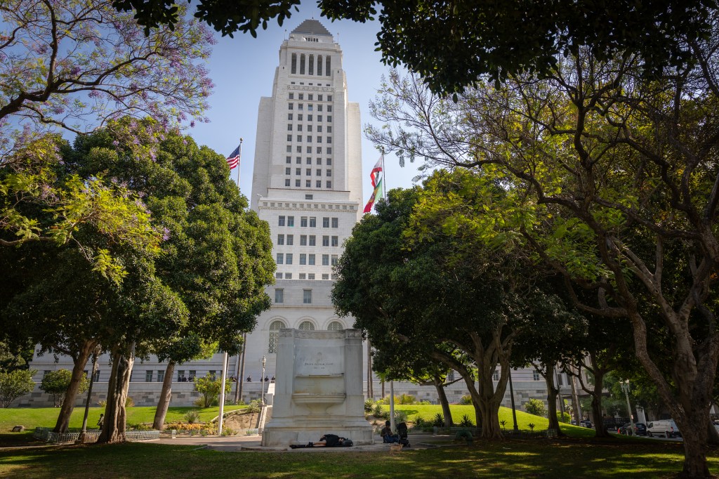 Unhoused people sleep and rest on a non-functioning fountain in front of Los Angeles City Hall.