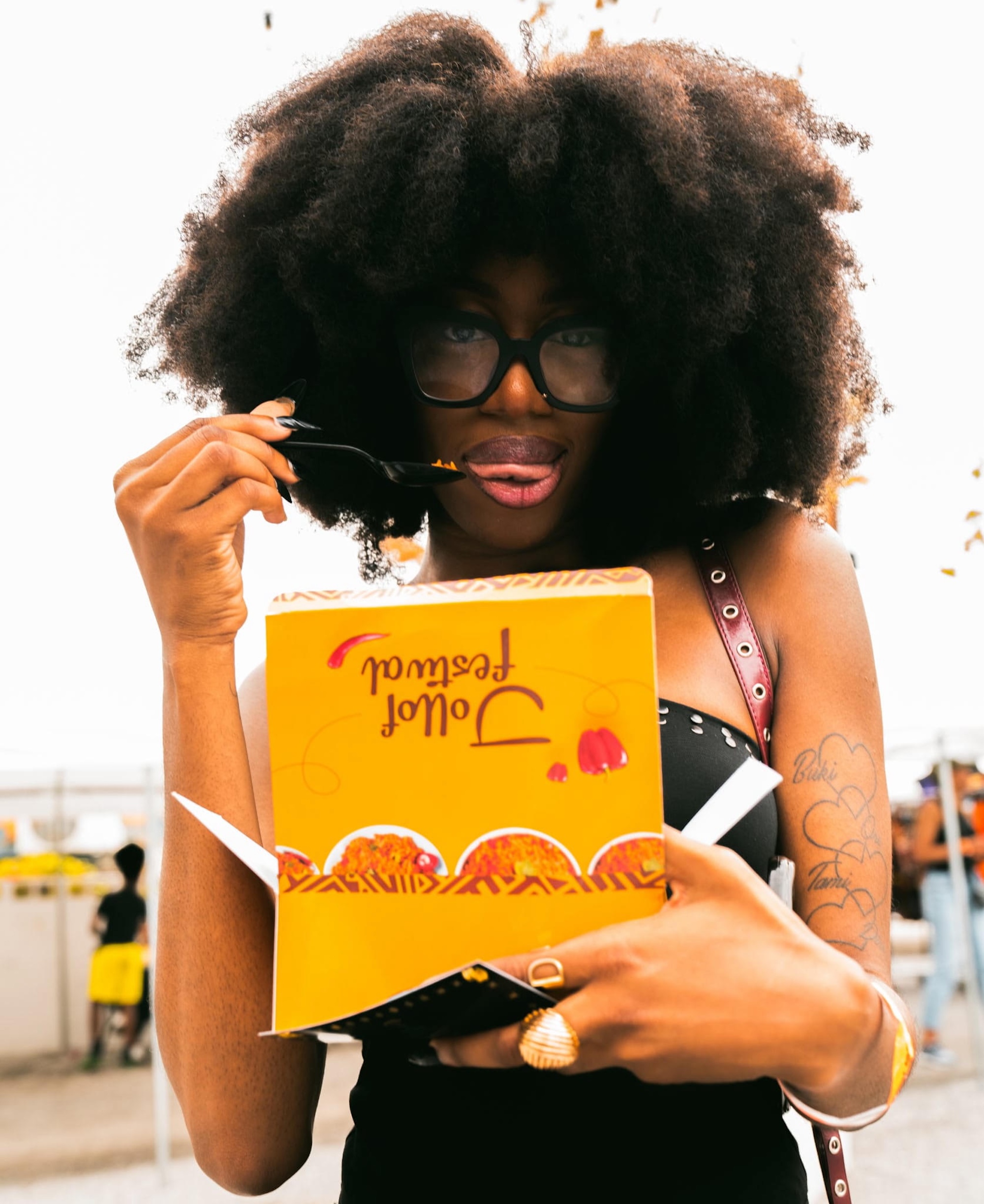 A woman holding a yellow box of food that reads "Jollof Festival" on the top of it.