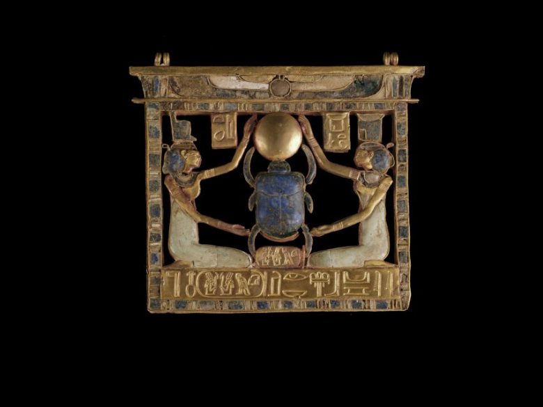 Ancient Egyptian gold and stone pendant depicting two figures holding a scarab beetle and sun disk, with hieroglyphic inscriptions below.