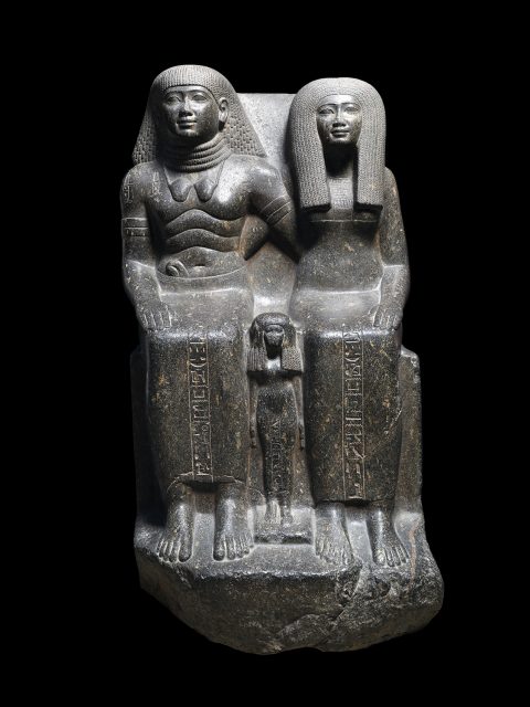 Ancient Egyptian stone statue depicting two seated adults and a small child standing between them, all with hieroglyphic inscriptions on their garments.