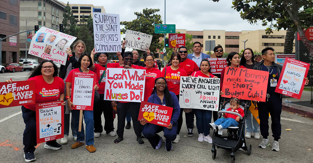 Large group of nurses outside hospital holding signs calling for patient safety and other measures