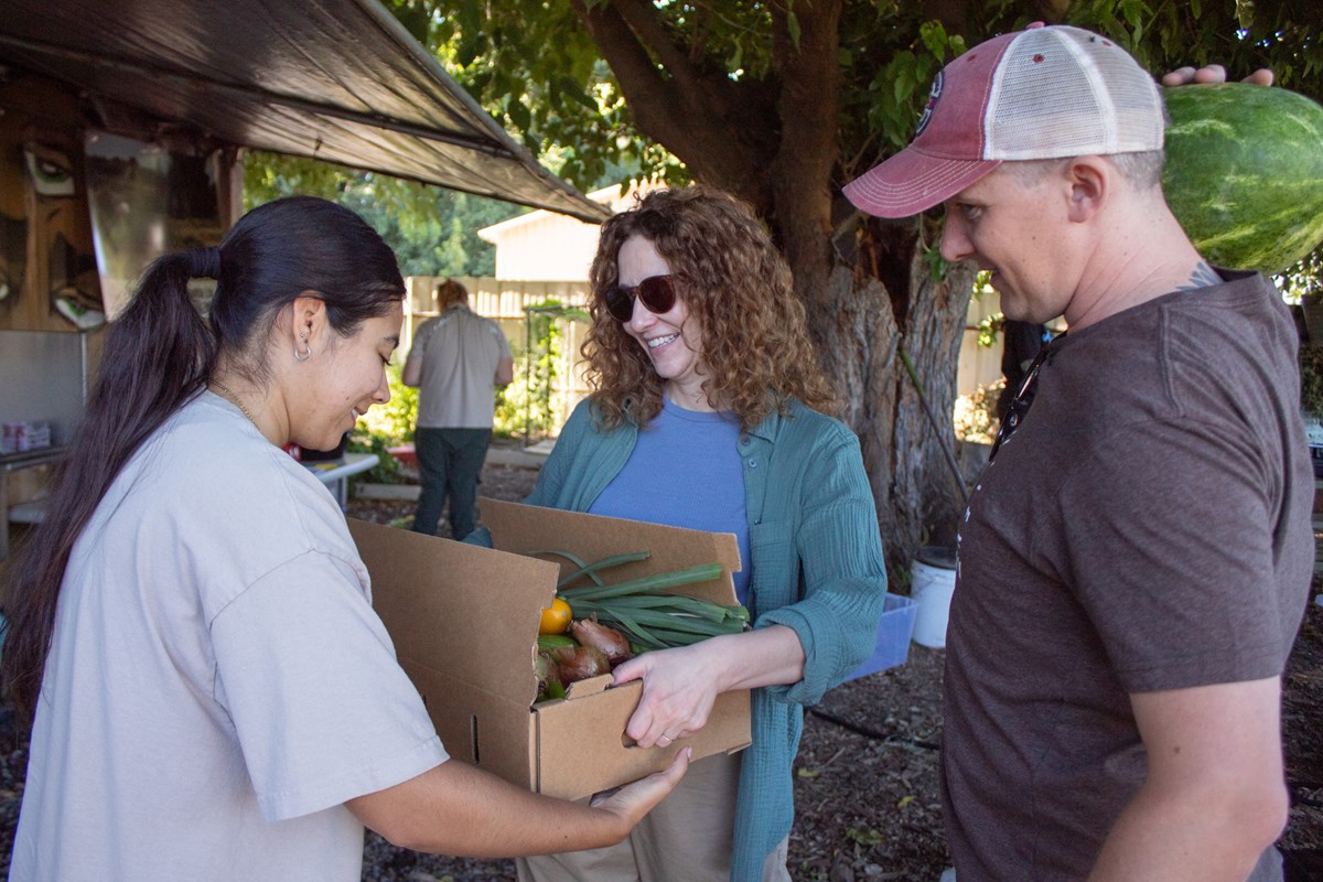 Farm hand Fatima Arriaga hands a CSA box to Lauren Foster and Jared Weathers Friday, July 24, 2026, at Three Sisters Gardens in West Sacramento.