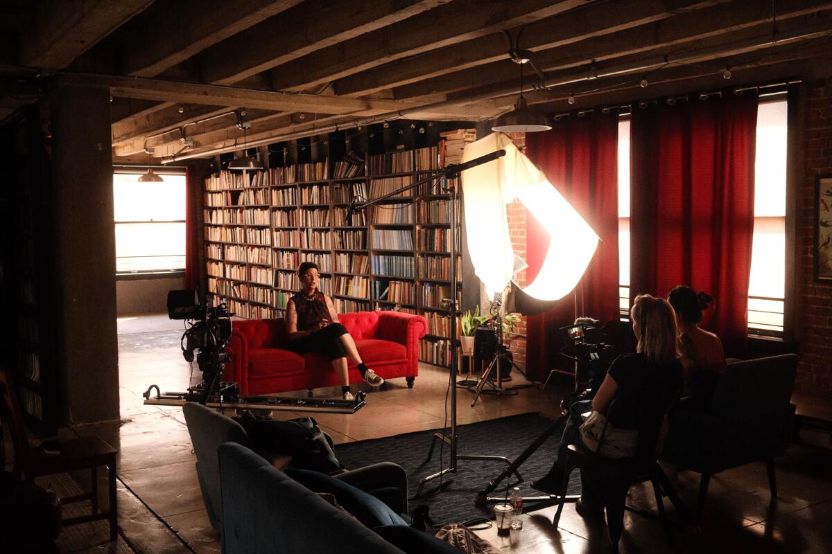Two women sit behind microphones and interview a woman on a red couch.