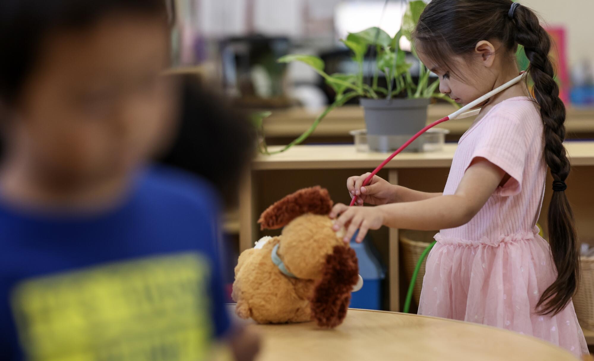A child wearing a stethoscope around her neck checks on a stuffed dog.