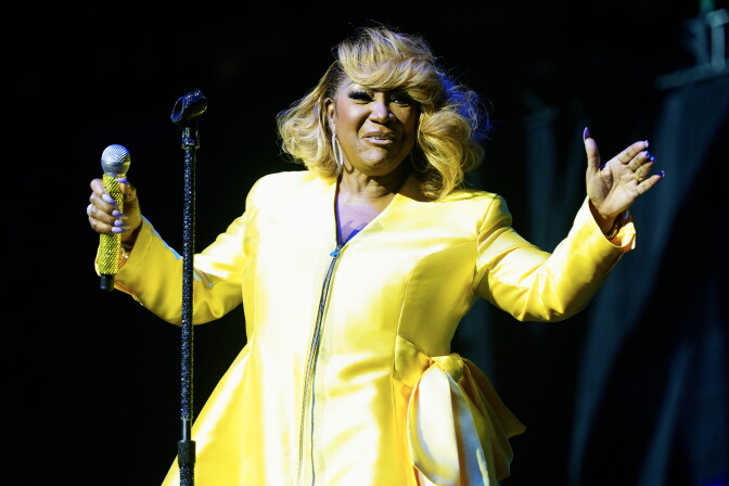 A medium-dark-skinned woman in a yellow suit holds a microphone onstage.