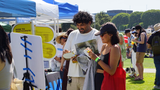 A medium-dark-skinned man in a white t-shirt and a medium-light-skinned woman in a black hat write on small pads.
