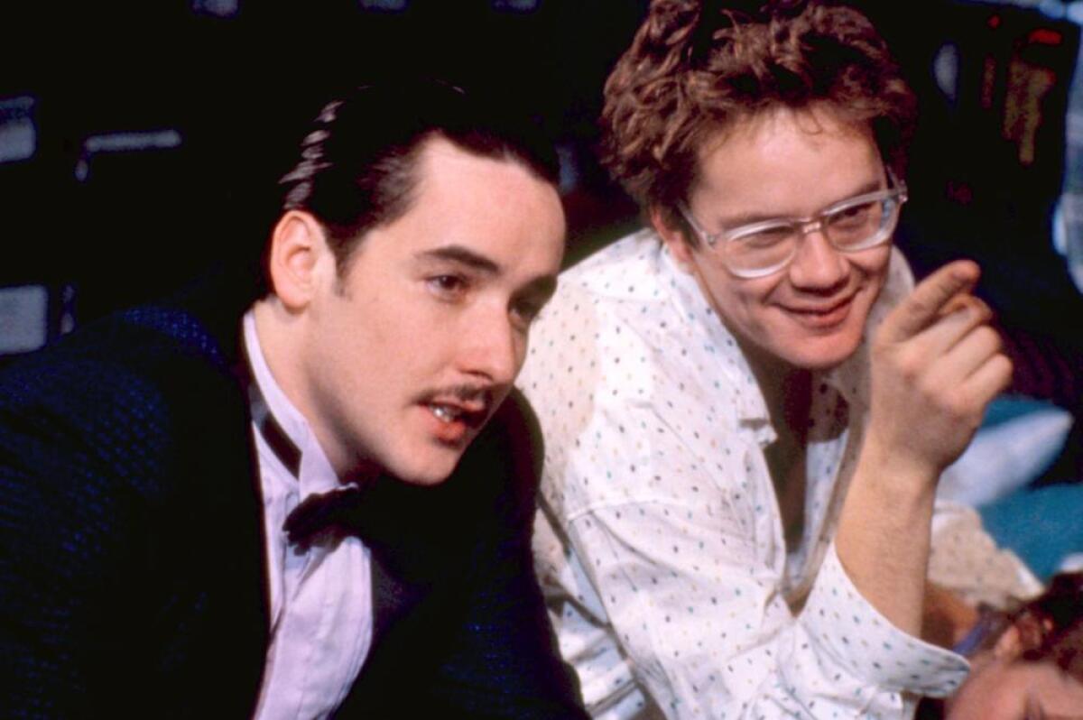 A man in a tuxedo plans with someone wearing glasses.