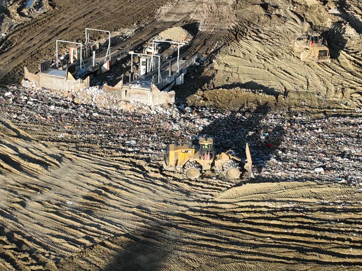 An aerial view of trucks unloading, heavy equipment spreading trash over a hill  at Chiquita Canyon Landfill.