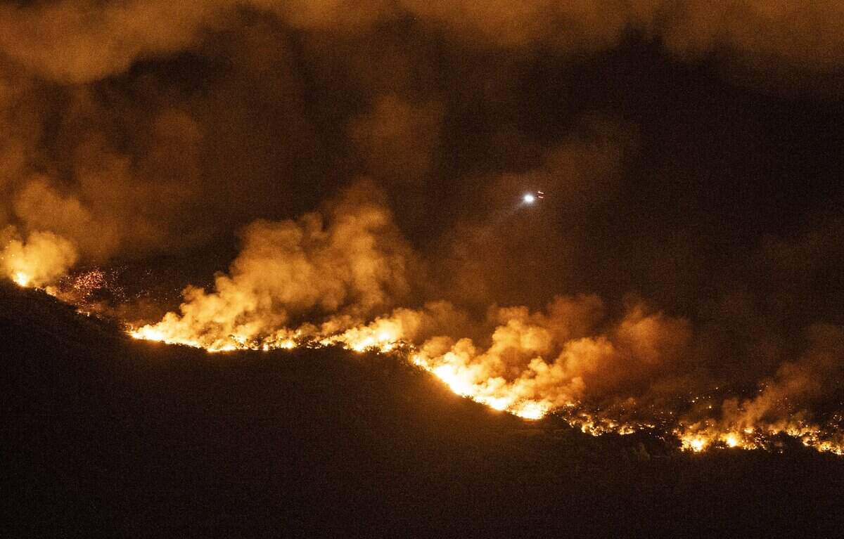 A helicopter flies over the Gann Fire in Calaveras County near New Hogan Reservoir, as seen from Hogan Dam Road, on Tuesday. The fire has burned more than 10,000 acres and killed one resident.