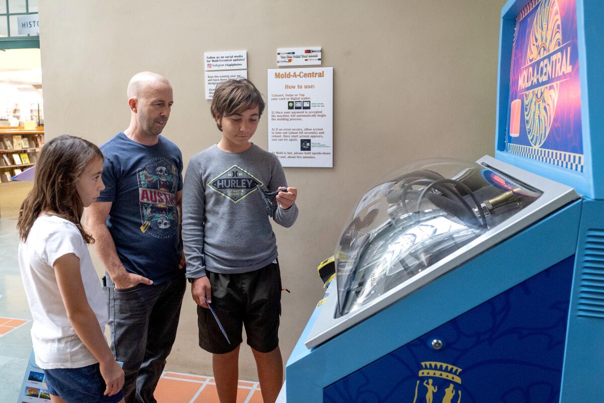 A dad and his son and daughter look at a sphinx made at a blue vending machine.