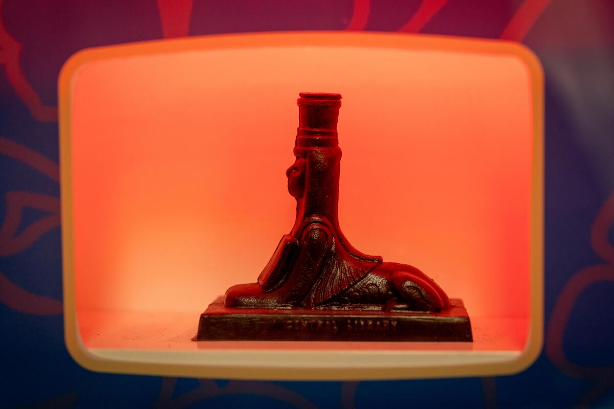 A black sphinx souvenir stands sideways inside a vending machine's delivery box.