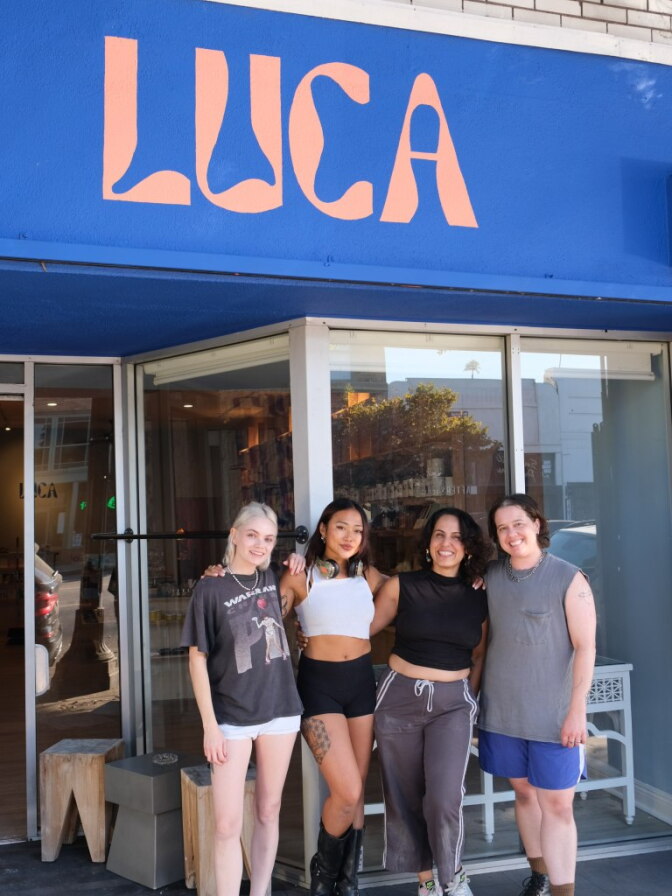 Three people stand outside posing for a photo in front of a storefront window.