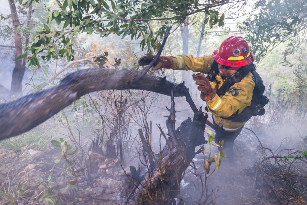 A firefighter throws a burning log out of the way while fighting the Timber Fire above Deetjen's Inn in Big Sur, Calif., Tuesday, Aug. 11, 2026. (AP Photo/Nic Coury)
