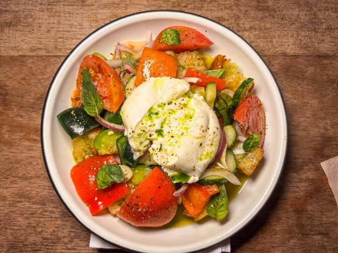 An overhead shot of a panzanella salad with heirloom tomatoes, cucumber, red onion, and torn bread, topped with a mound of burrata drizzled in olive oil.
