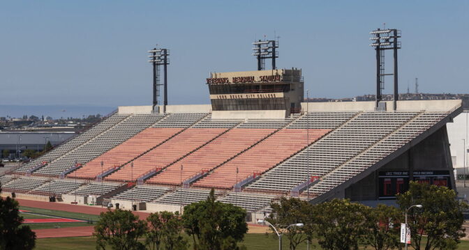 Large stands face a football and track field with signage on it that reads "Veterans Memorial Stadium."