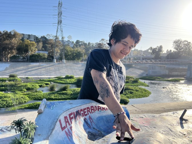 Darren Mojica performs a trick on the quarter pipe ramp that Ryan Diaz painted. It depicts a "Jaws" like shark with the words "LA FINGERBOARD MECCA" around it. The LA River and 5-freeway are seen in the background.