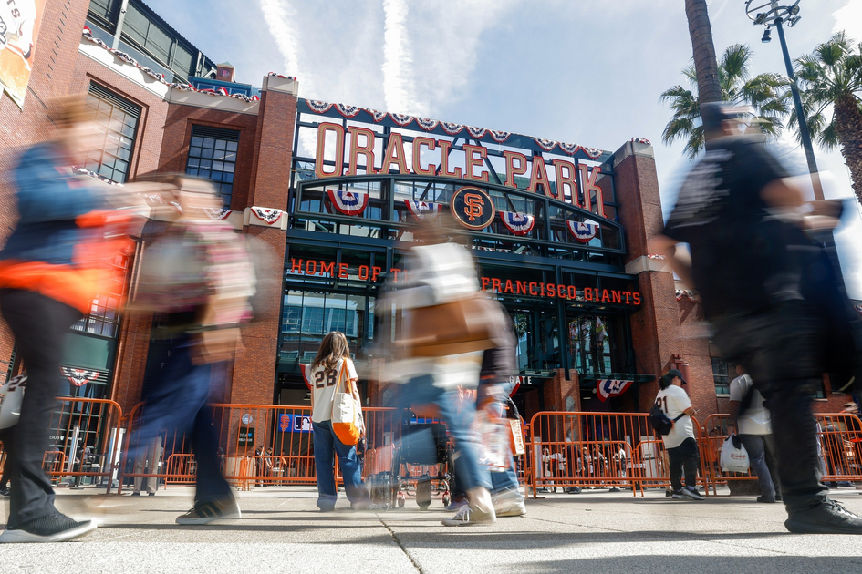 Oracle Park entrance is decorated with banners, with people walking by and some wearing San Francisco Giants jerseys.