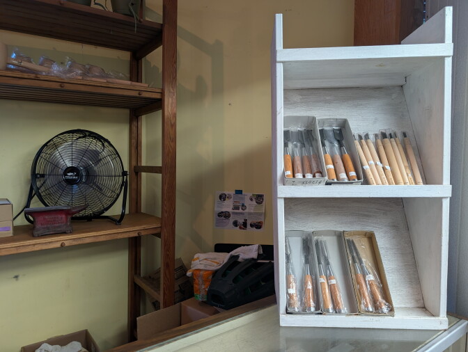 A wooden shelf with a vintage fan is next to a smaller shelf with wooden chisels.
