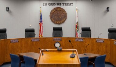 A empty government meeting room with a wooden table, chairs, and a seal on the wall.